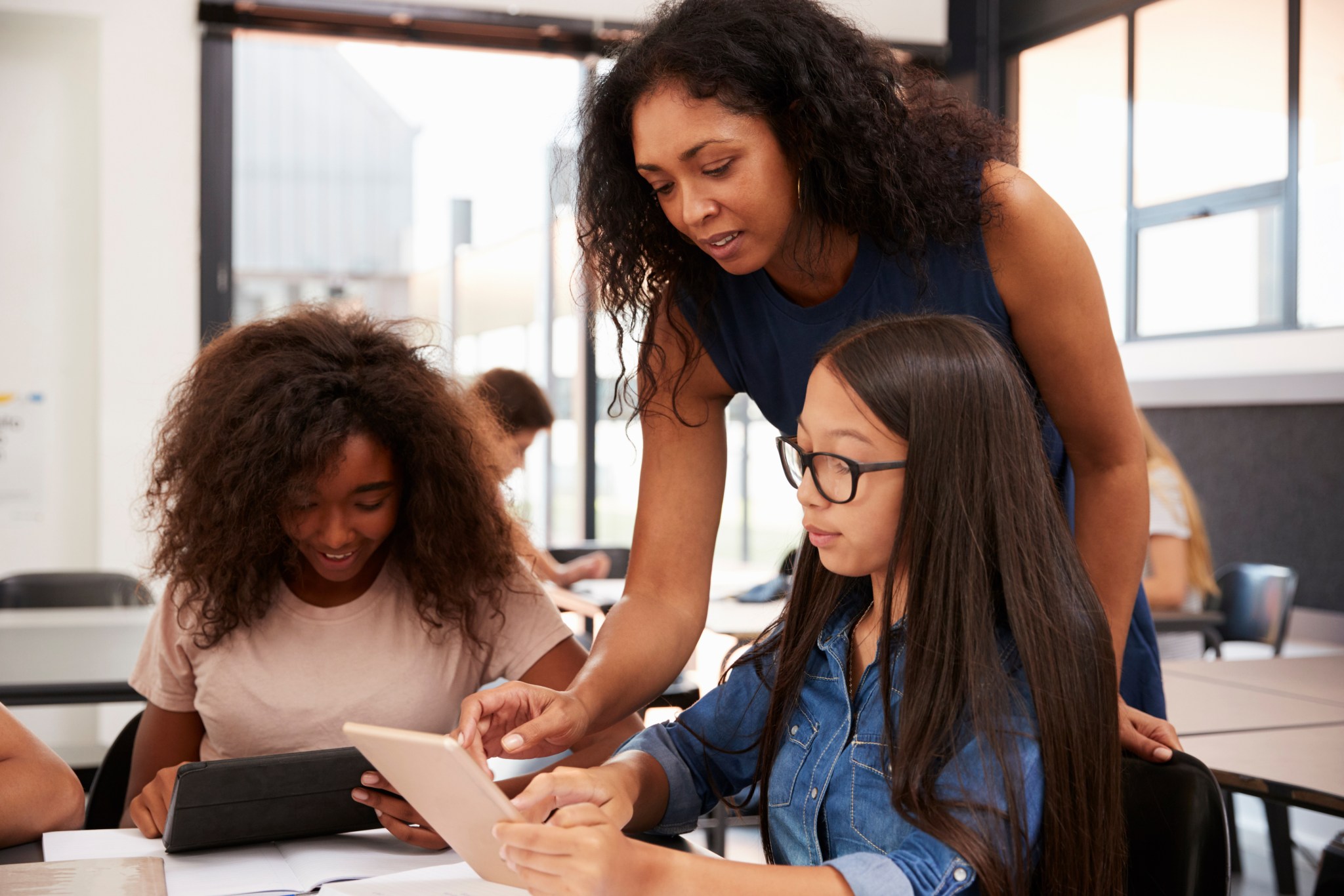 A teacher guides high school students as they work with education technology in a classroom.